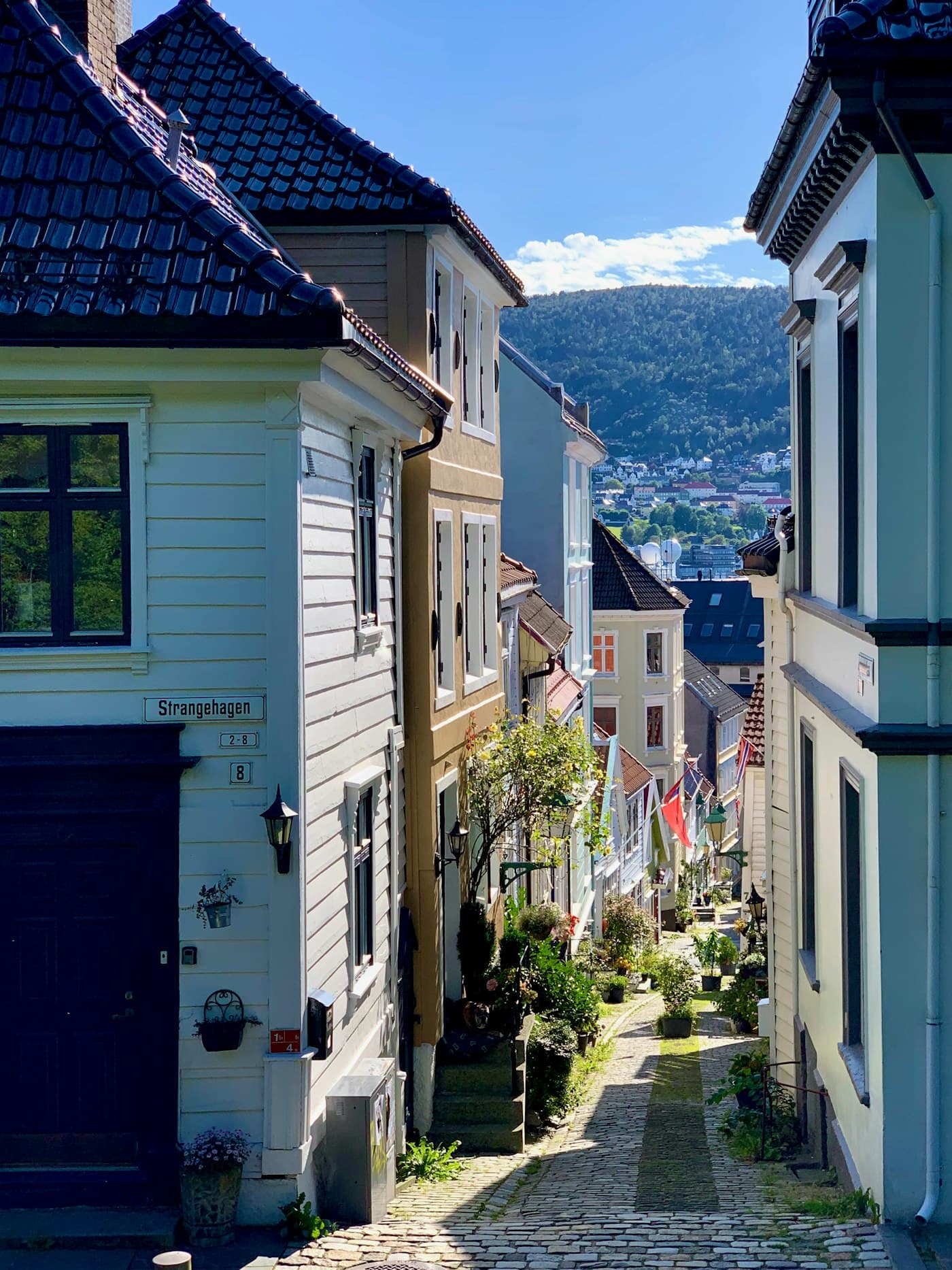 Strangehagen i Bergen: en smal brosteinsgate med hvite trehus og fjellet i bakgrunnen